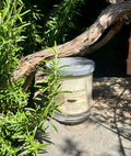 Vanilla Soy Candle in a glass jar with a wooden lid on a stone surface with greenery